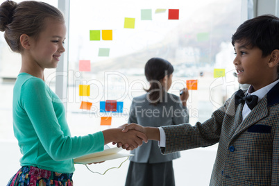 Colleagues shaking hands while businesswoman working in background