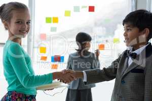 Smiling colleagues shaking hands while businesswoman working in background