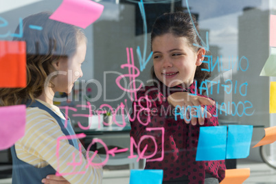 Smiling female coworkers anlayzing data seen through glass