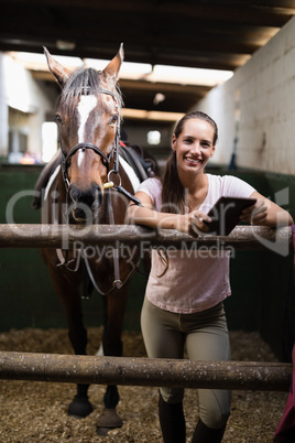 Portrait of smiling female jockey using digital tablet by standing by horse