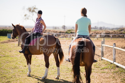 Female friends horseback riding on field