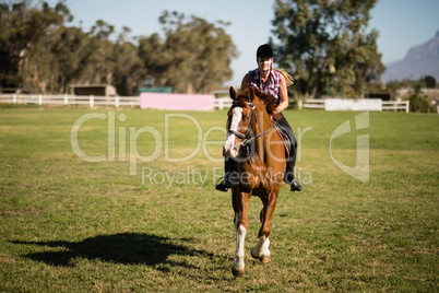 Full length of female jockey horseback riding on field