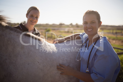 Portrait of smiling female jockey and vet standing by horse