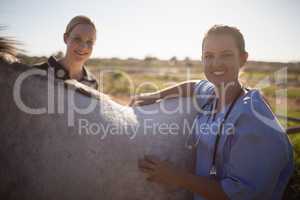 Portrait of smiling female jockey and vet standing by horse