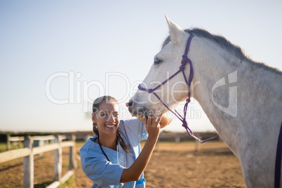 Smiling female vet eaxmining horse at barn