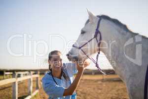 Smiling female vet eaxmining horse at barn