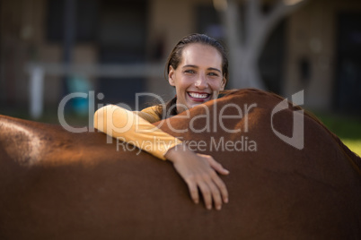 Smiling female jockey leaning on horse at barn