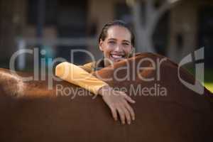 Smiling female jockey leaning on horse at barn