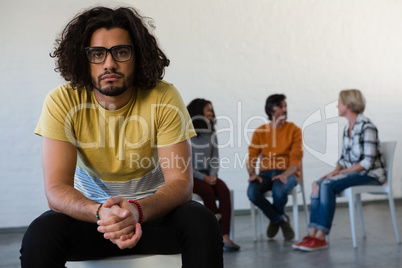 Portrait of man sitting on chair with friends discussing in background
