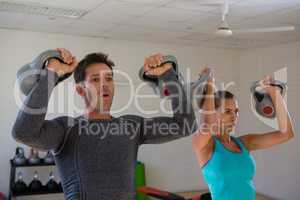 Confident trainer with athlete lifting kettlebells in health club