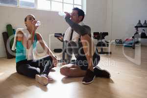 Tired athletes drinking water while sitting in gym