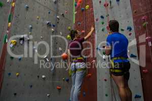 Male trainer guiding woman in climbing wall at club