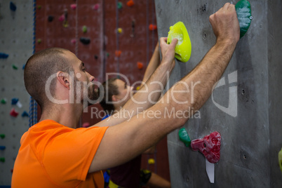Male trainer guiding athlete in climbing wall at health club