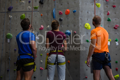 Rear view of trainer with athletes standing by climbing wall