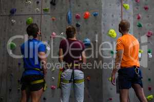 Rear view of trainer with athletes standing by climbing wall