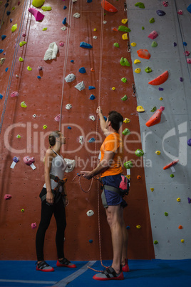 Male trainer assisting female athlete in climbing wall at gym