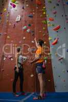 Male trainer assisting female athlete in climbing wall at gym