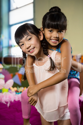 Girl giving piggyback ride to her friend during birthday party