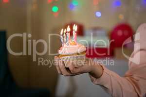 Girl holding cupcake with lit candle during birthday party