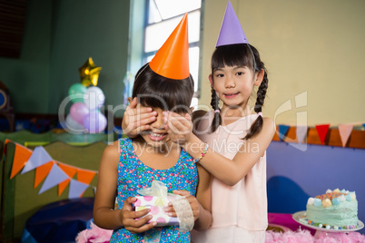 Girl covering birthday girls eyes and offering a gift