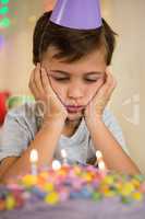 Upset boy sitting with birthday cake