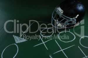 American football head gear lying on green board with strategy drawn on it