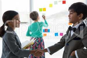 Business people shaking hands while businesswoman working in background