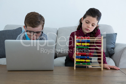 Businessman using laptop while female colleague counting with abacus