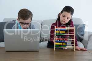 Businessman using laptop while female colleague counting with abacus