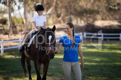 Smiling female jockey holding bridle while sister sitting on horse