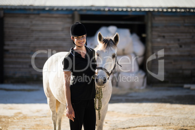 Confident female jockey standing by white horse at barn