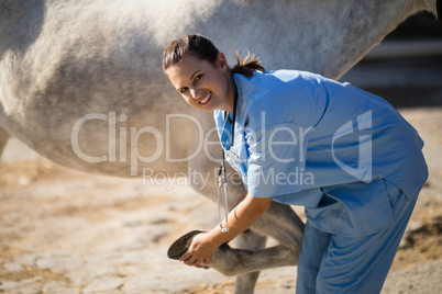 Portrait of smiling vet examining horse hoof at barn