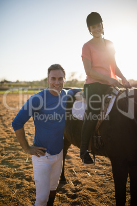 Portrait of trainer standing by young woman sitting on horse