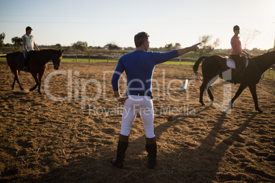 Male trainer guiding young women in riding horse