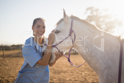 Smiling female vet stroking horse at barn