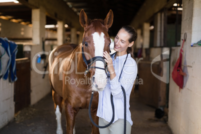 Smiling vet strocking horse in stable