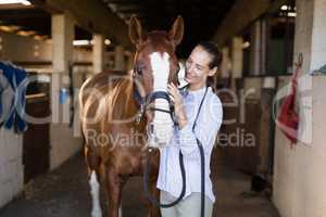 Smiling vet strocking horse in stable