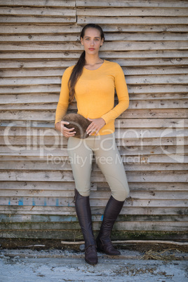 Confident female jockey standing against wooden wall