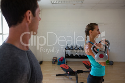 Male trainer looking at female athlete lifting kettlebells