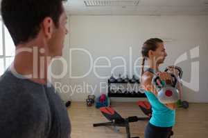Male trainer looking at female athlete lifting kettlebells