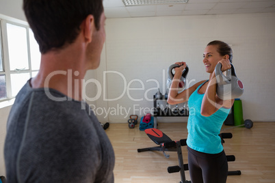 Trainer looking at female athlete lifting kettlebells at club