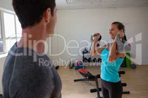 Trainer looking at female athlete lifting kettlebells at club