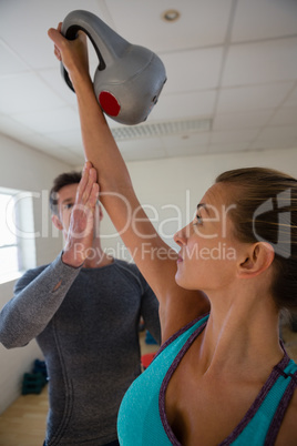 Trainer assisting female athlete in lifting kettlebells at club