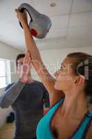 Trainer assisting female athlete in lifting kettlebells at club