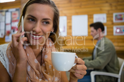 Close up of young woman talking on smart phone with man in background
