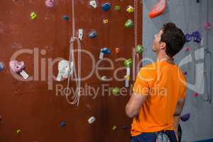Rear view of young man looking up while standing by climbing wall