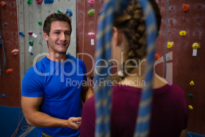 Smiling trainer guiding female athlete in wall climbing
