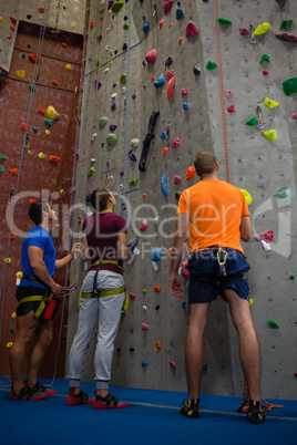 Trainer with athletes standing by climbing wall at gym