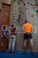 Trainer with athletes standing by climbing wall at gym
