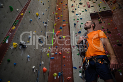 Low angle view of trainer with rope standing by climbing wall in gym
